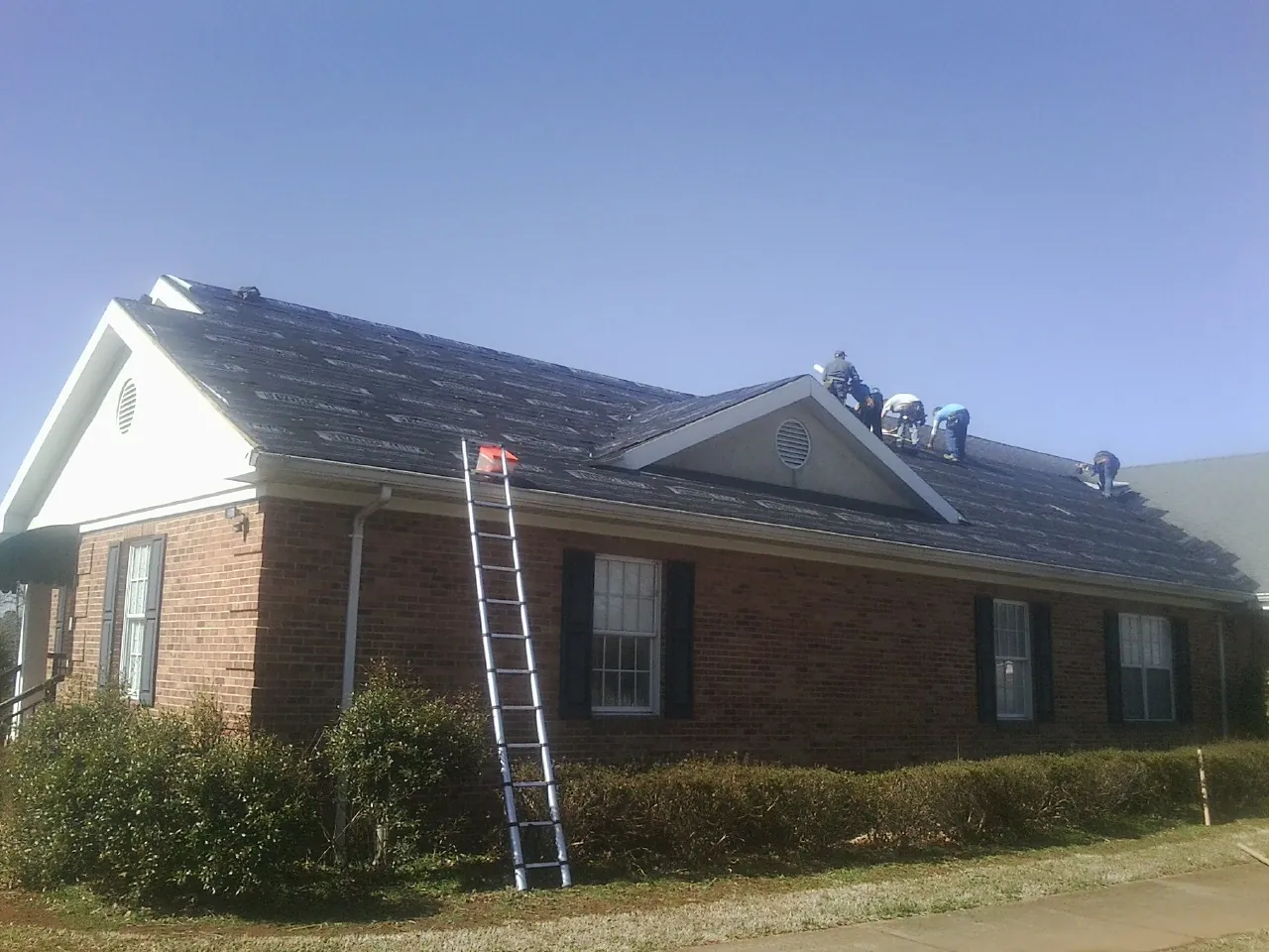 Crew tearing shingles off a brick ranch roof with a ladder set — Emergency Roof Repair work by our crew in Sumatra