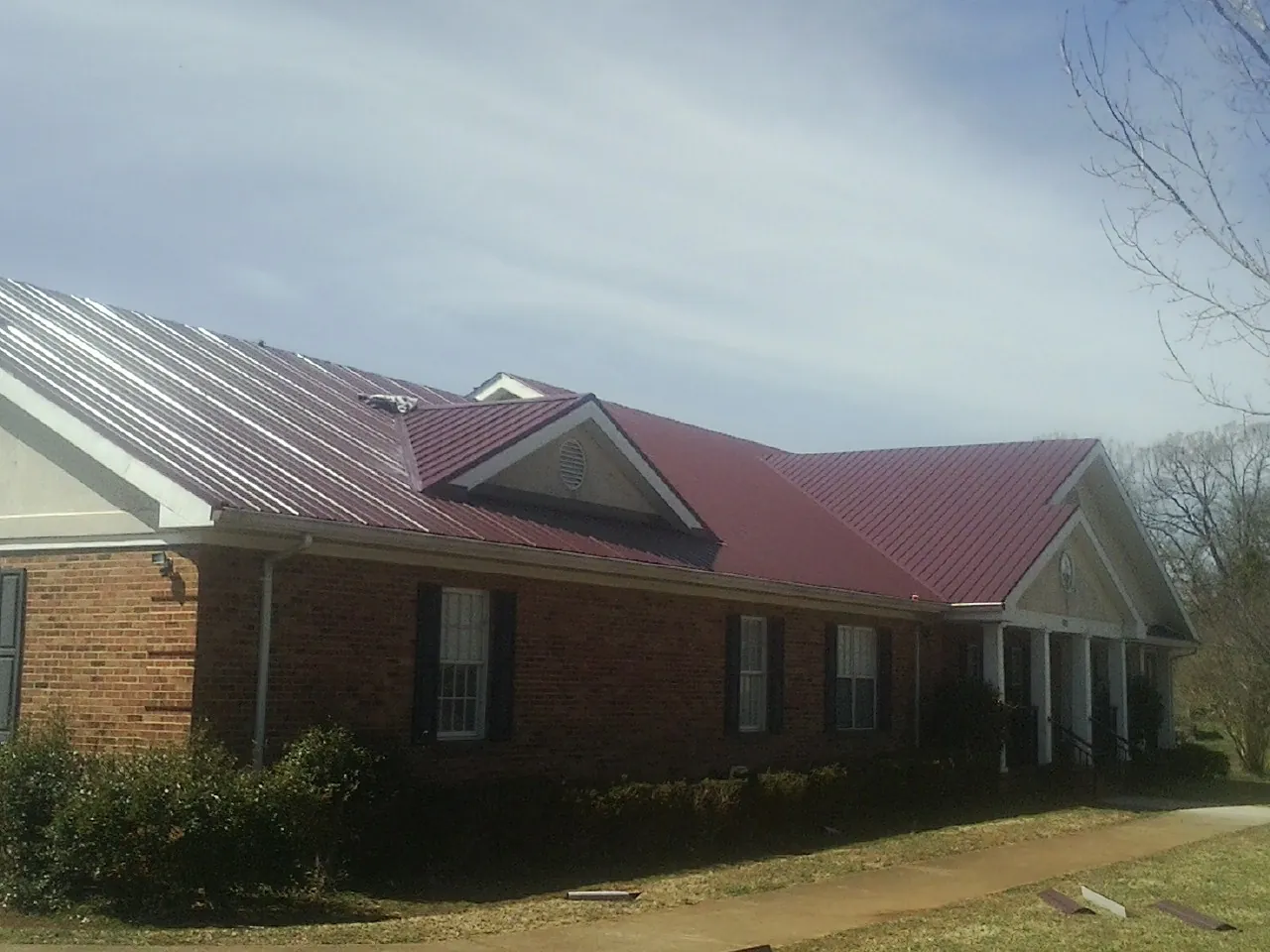 Red metal roof with gabled entries on a long brick building, from a Hail Damage Roof Repair job in Sumatra