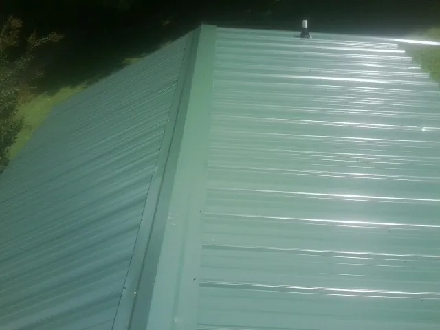New green metal panels meeting at the ridge of a roof — Flat Roof Repair work by our crew in Sumatra