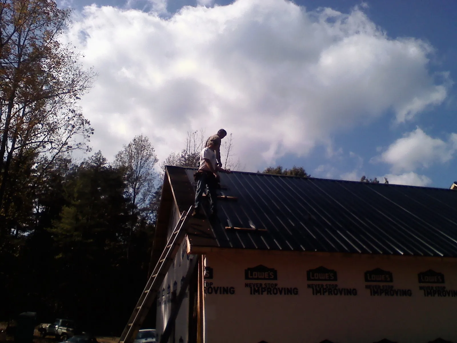Roofer fastening dark metal panels high against a cloudy sky, from a Roof Inspection job in Sumatra